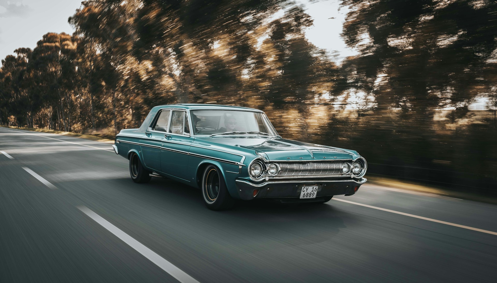 Blauwgroene klassieke Dodge rijdend over een bosweg